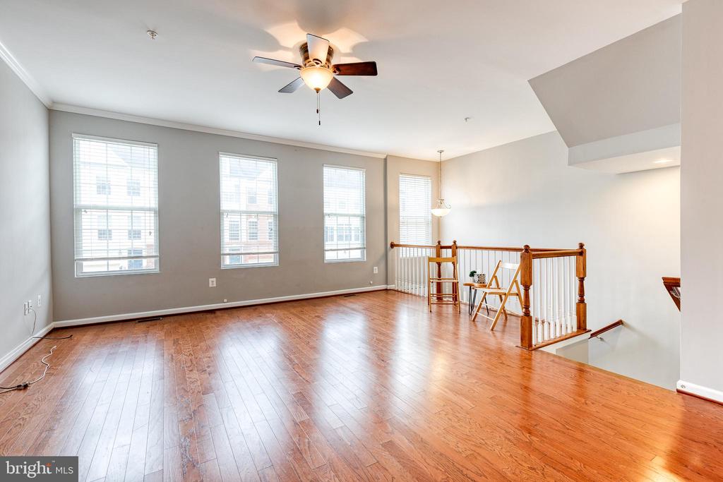 Open upstairs living area with hardwood floors, tall windows, ceiling fan, and stair railing.