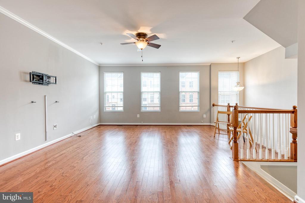 Mostly empty living room with hardwood floors, three tall windows, and a wooden staircase railing.