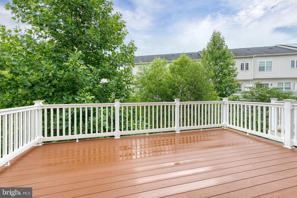 Spacious brown deck with white railings overlooking leafy trees and neighboring townhouses.