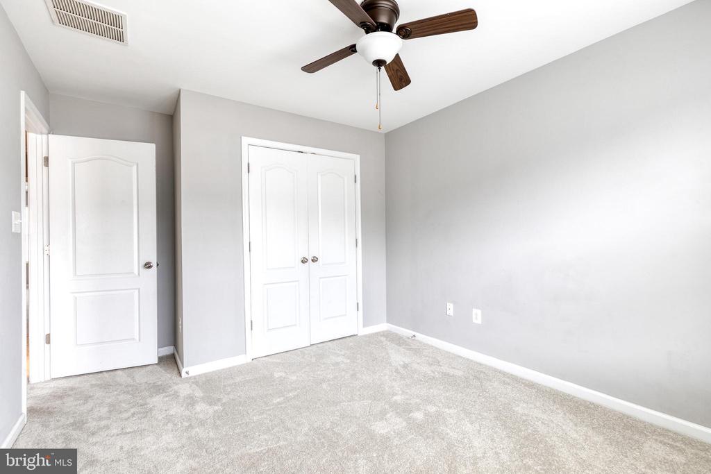 Vacant bedroom with wall-to-wall carpet, white double closet doors, and a dark wood ceiling fan.