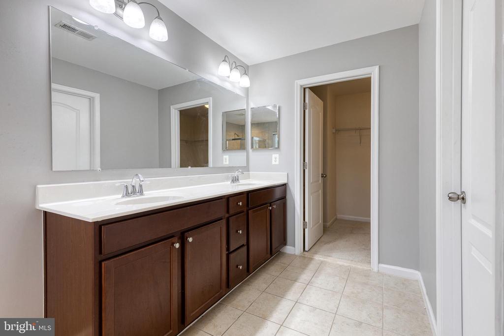Bathroom with a long double vanity, large mirror, and doorway to a walk-in closet.