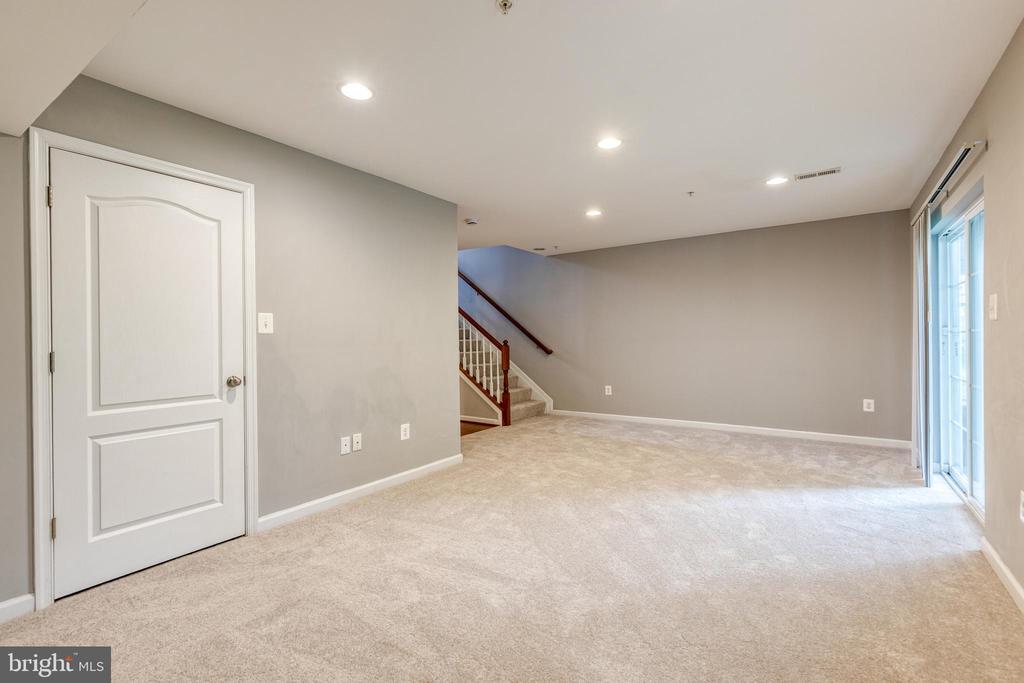 Empty carpeted lower-level room with a staircase and sliding glass doors.