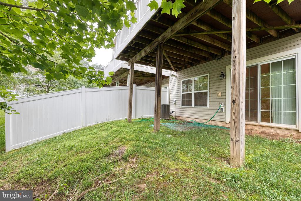 Backyard with a raised deck overhead, white privacy fence, and sliding glass doors.