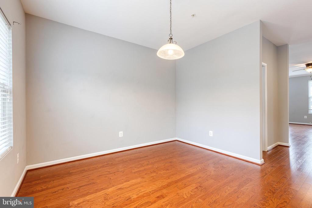 Vacant dining area with hardwood floors, a pendant light, and a window with white blinds.