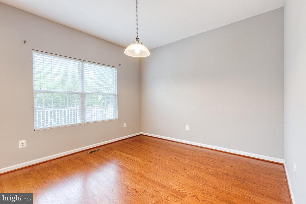 Empty dining room with hardwood floors, a large blinded window, and a hanging pendant light.