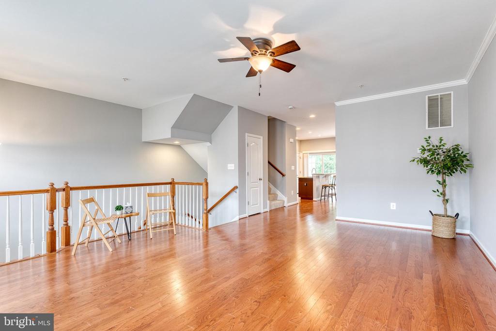 Living area with hardwood floors, a ceiling fan, and a wooden railing overlooking the stairs.