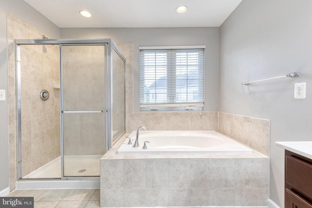 Bathroom with a built-in soaking tub beside a glass-enclosed tiled shower and window.