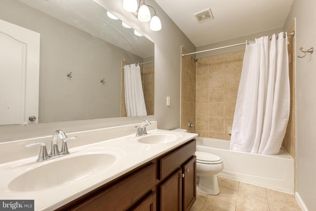 Bathroom with a double vanity and a bathtub with beige tile surround.