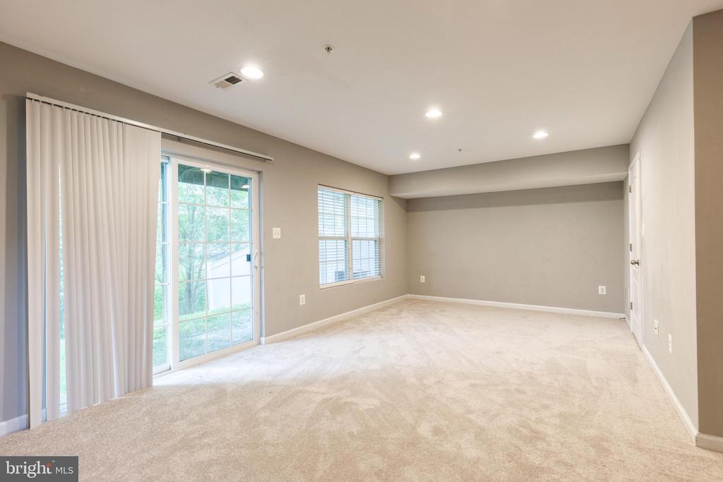 Empty carpeted room with beige walls, recessed lights, and a sliding glass door.