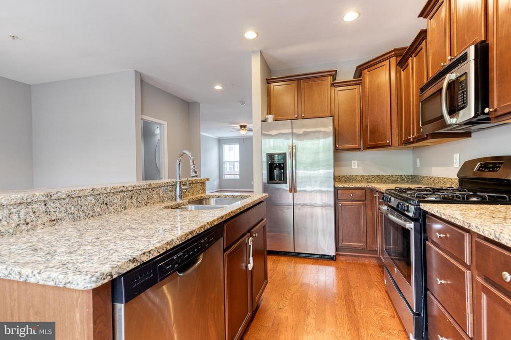 Kitchen with granite counters, warm wood cabinets, stainless steel appliances, and hardwood floors.