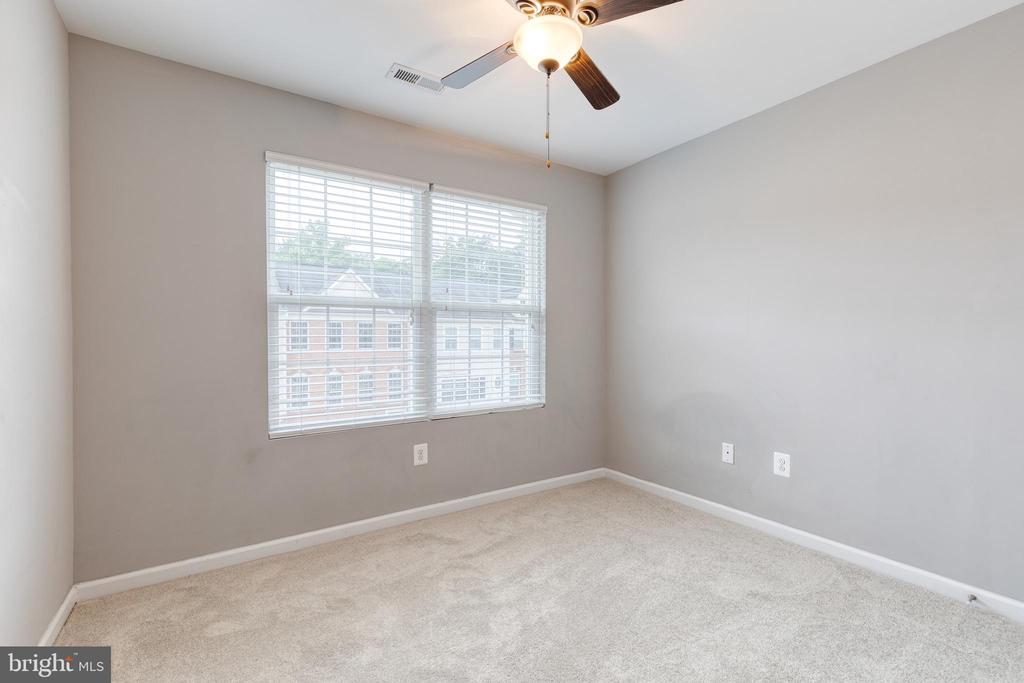 Empty bedroom with beige carpet, a ceiling fan, and a wide window with white blinds.
