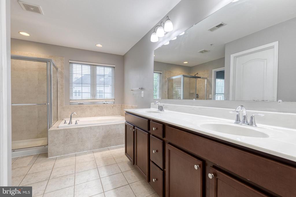 Primary bathroom with a dark double vanity, tiled soaking tub, and glass-enclosed shower.