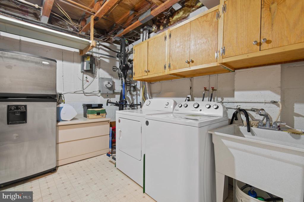 Laundry room with washer and dryer, utility sink, refrigerator, and overhead wooden cabinets.