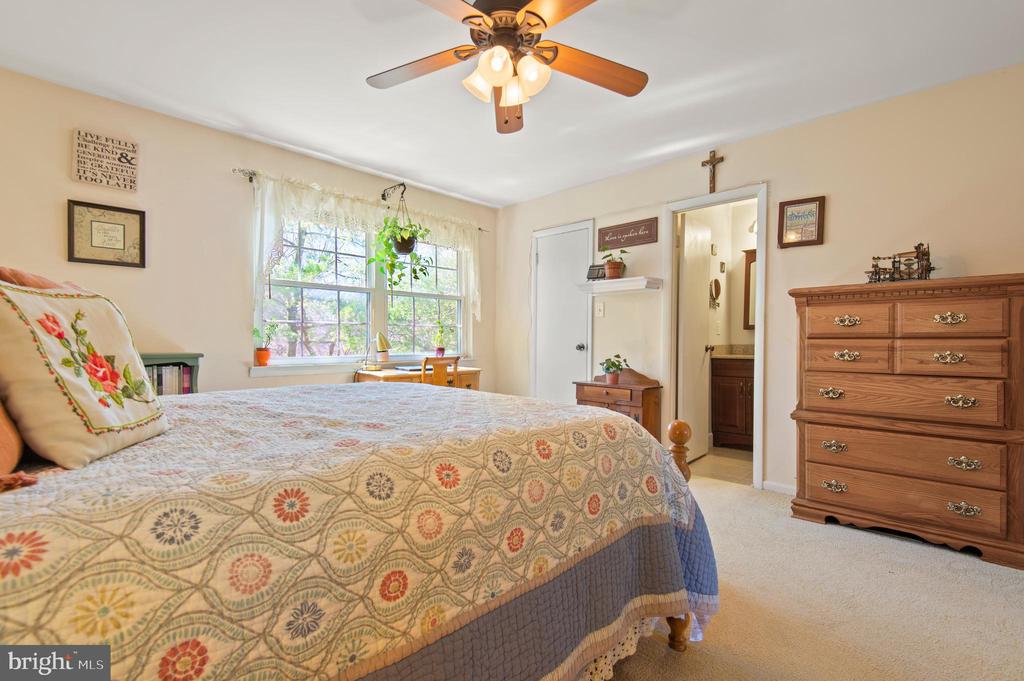 Furnished bedroom with a patterned quilt, ceiling fan, and large curtained window.