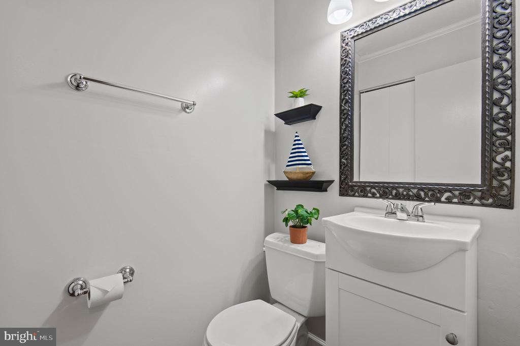 Bathroom with a white vanity and toilet, ornate mirror, and decorative shelves.