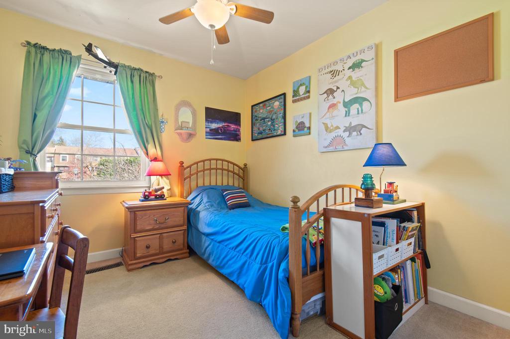 Bedroom with a wooden twin bed, bright blue bedding, dinosaur wall art, and a large window.