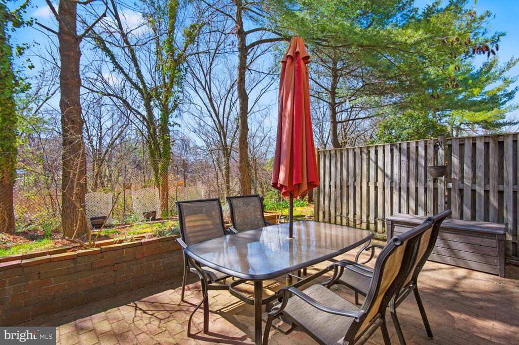 Patio dining set with a red umbrella beside a wooden privacy fence and wooded yard.