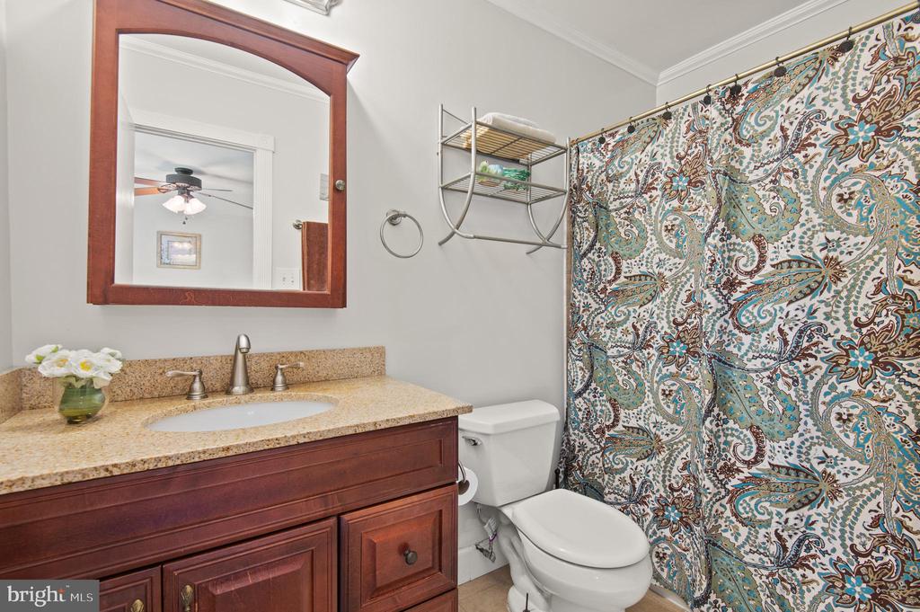 Bathroom with a granite-topped wood vanity and colorful patterned shower curtain.