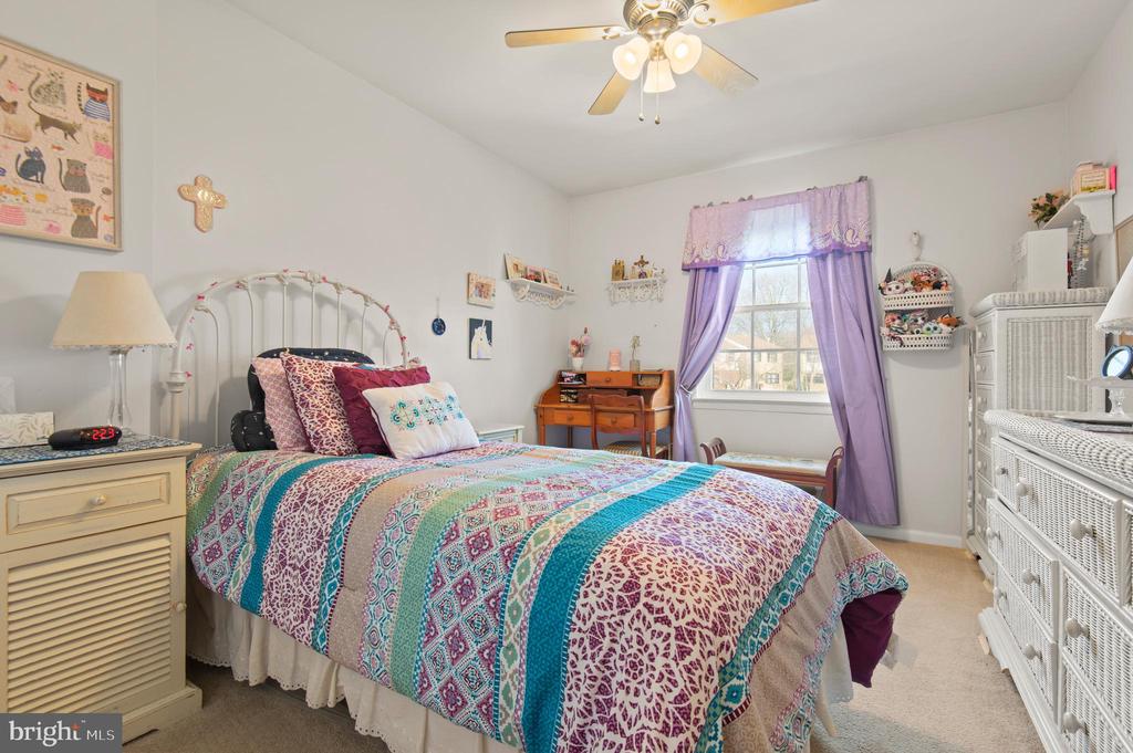 Bedroom with a colorful patterned quilt, purple curtains, and white wicker furniture.