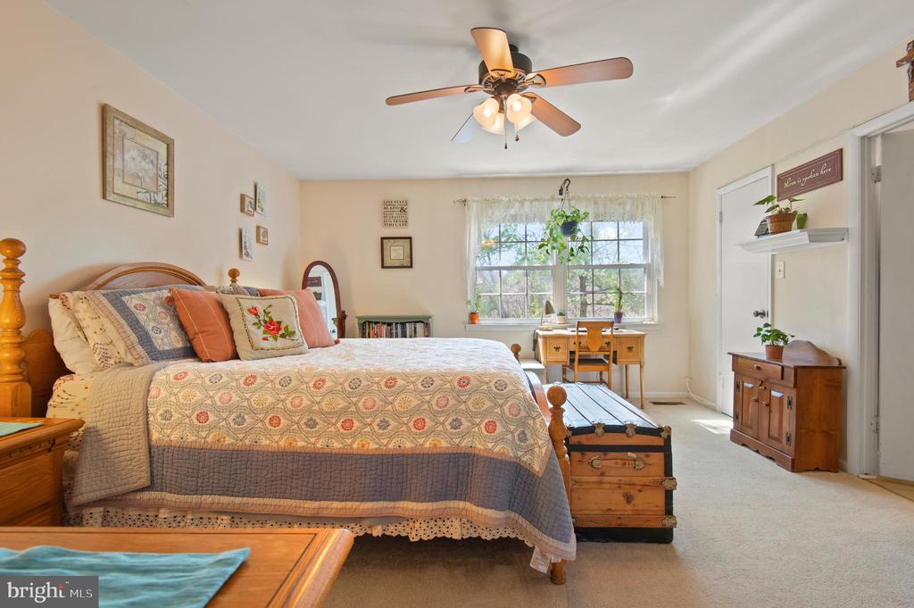 Furnished bedroom with a patterned quilt, wooden trunk, and desk by a sunlit window.