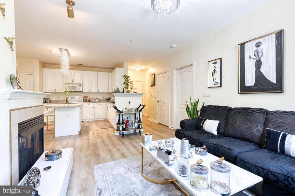 Open-plan living room and kitchen with white cabinets, a fireplace, and a dark patterned sofa.