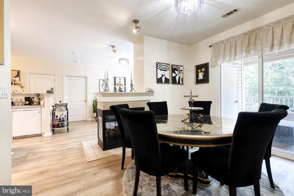 Dining area with a glass-top table, black chairs, tiled fireplace, and sliding doors to a balcony.
