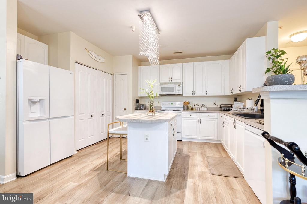 Bright kitchen with white cabinetry, central island, wood-look flooring, and a crystal pendant light.