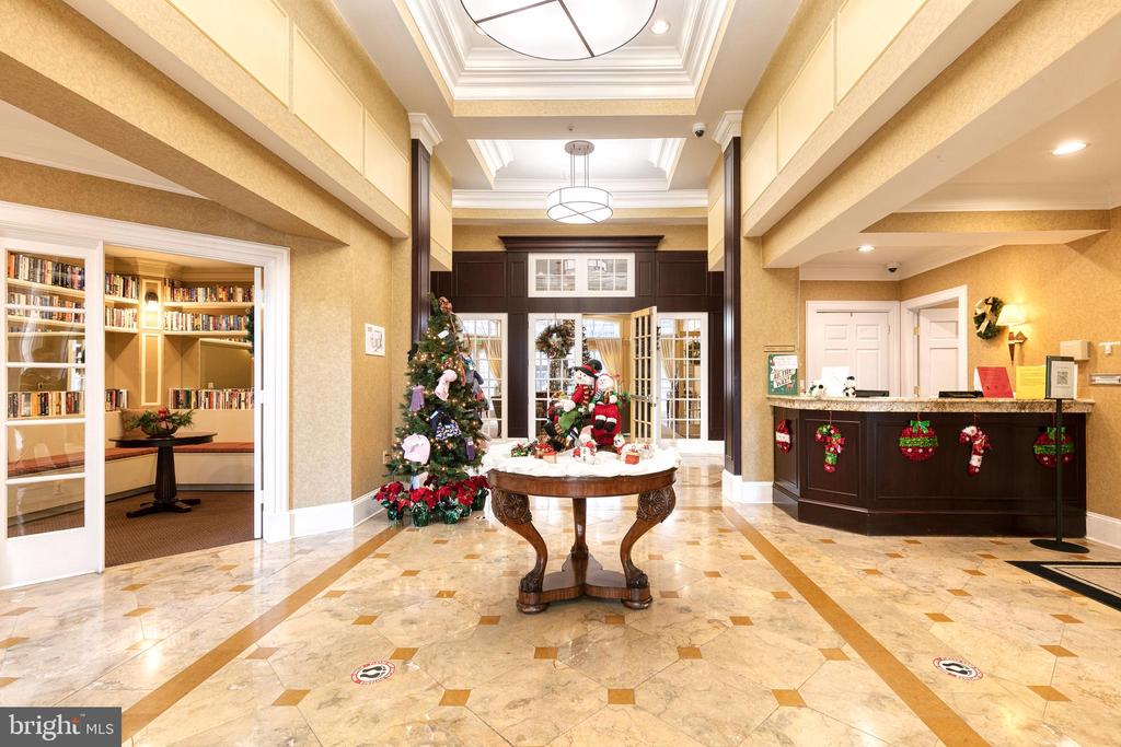 Building lobby with marble floors, a reception desk, and a Christmas tree beside a holiday display.