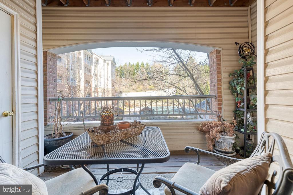Covered porch with a mesh table and cushioned chairs overlooking trees and neighboring buildings.
