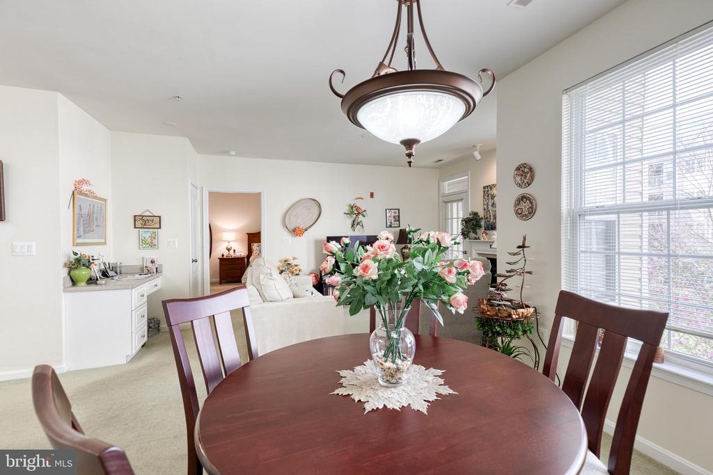 Dining area with a round wood table and floral centerpiece, open to a bright living room.
