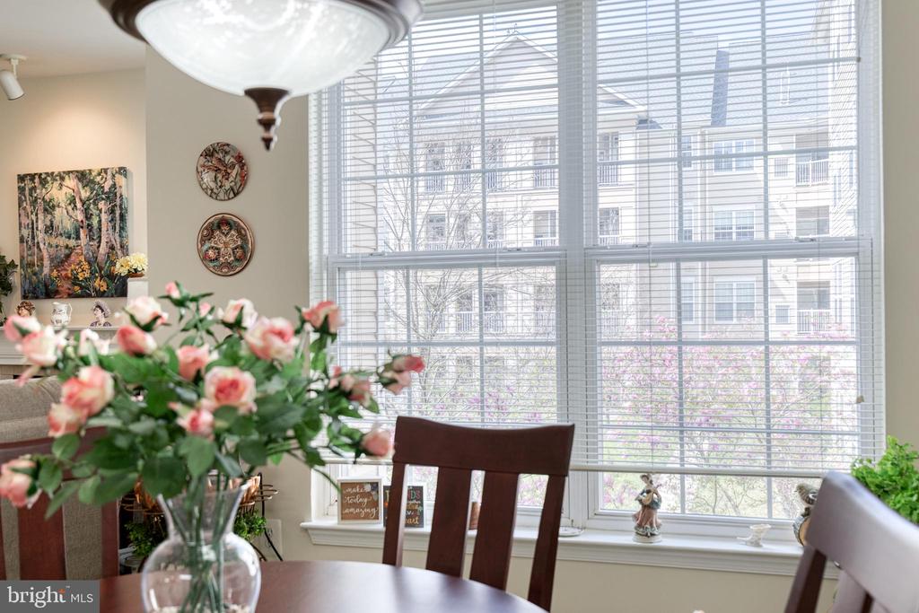 Dining area with a dark wood table, flowers, and large windows overlooking nearby buildings.