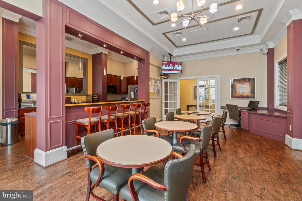 Communal dining room with round tables, gray chairs, and a kitchen bar with stools.