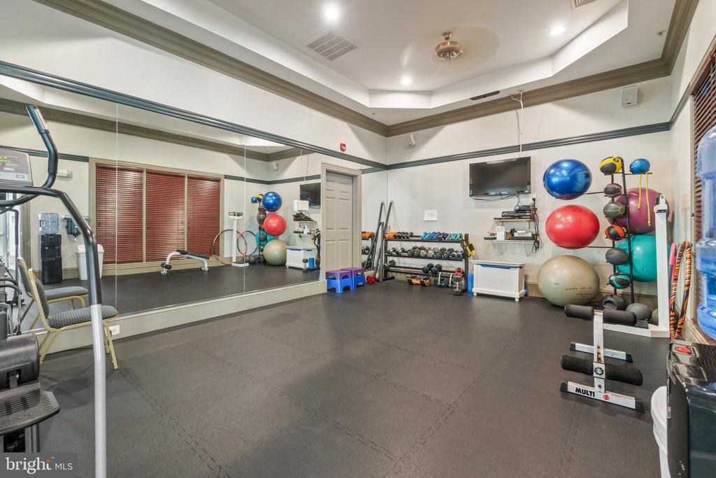 Fitness room with mirrored wall, weight racks, colorful exercise balls, and dark rubber flooring.