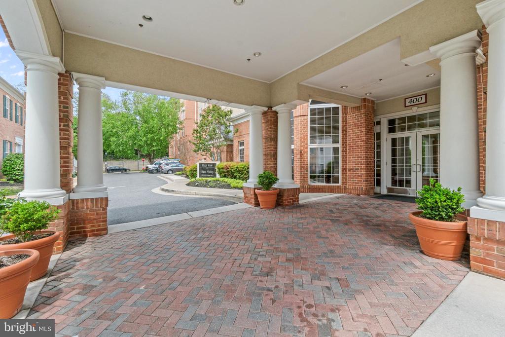 Covered brick-building entrance with white columns, glass doors, and brick paving.