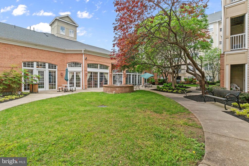 Residential courtyard with a brick clubhouse, green lawn, mature trees, and paved walkways.