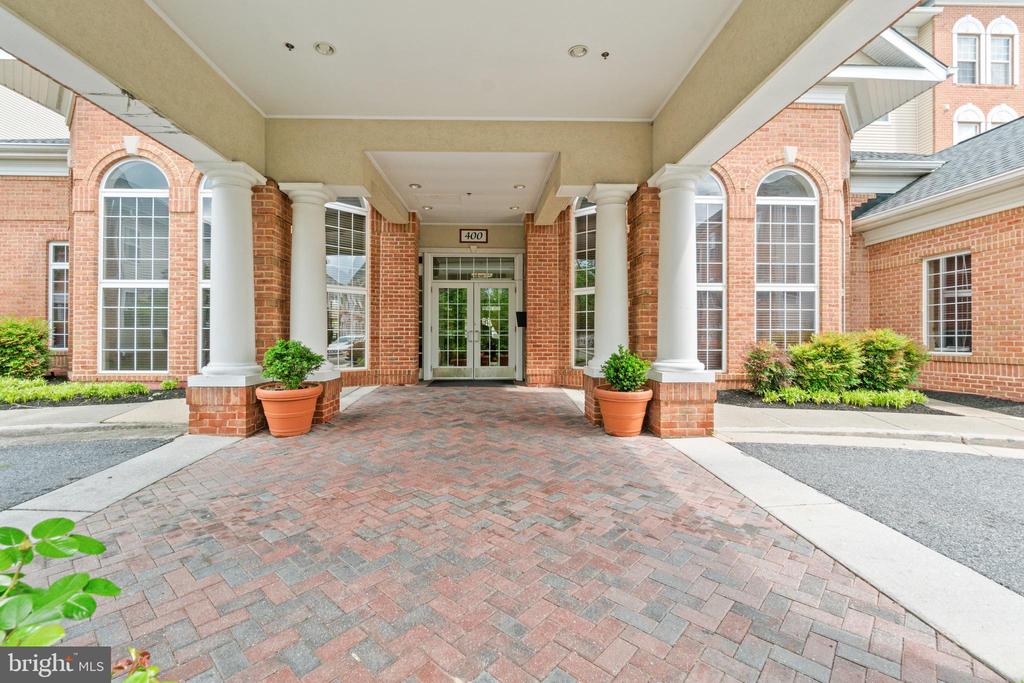 Building entrance with white columns, arched windows, and a brick-paved driveway.