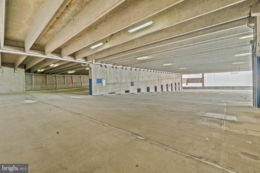 Covered parking garage with a broad concrete floor and exposed beams.