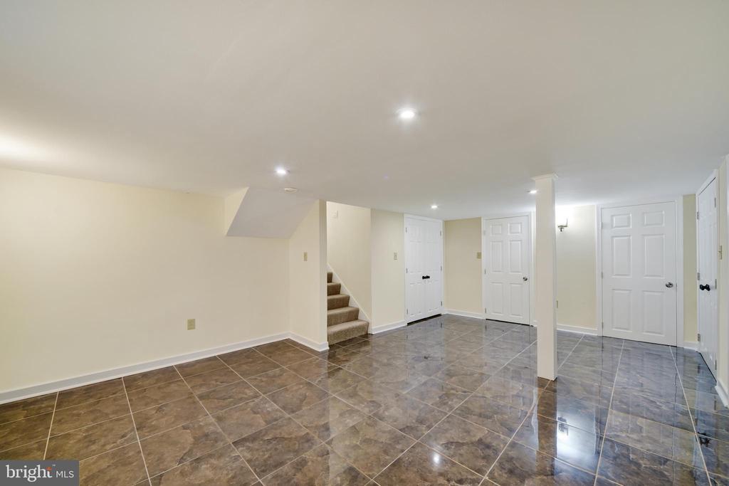 Vacant basement with glossy tile floors, recessed lights, and stairs.
