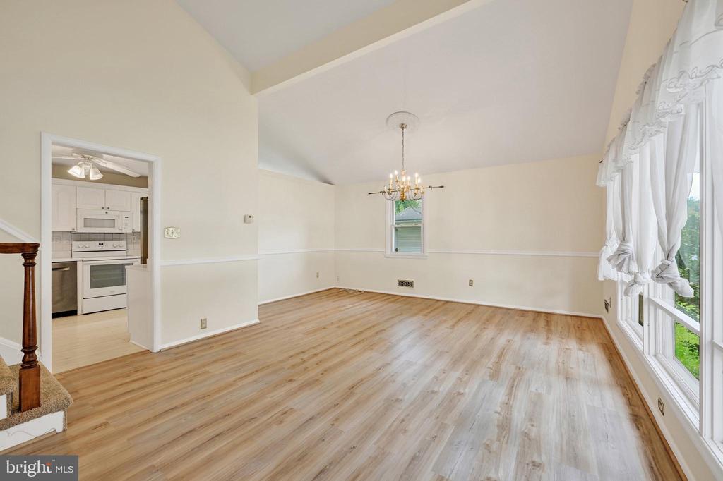 Dining room with light wood flooring, chandelier, tall windows, and an adjoining kitchen.