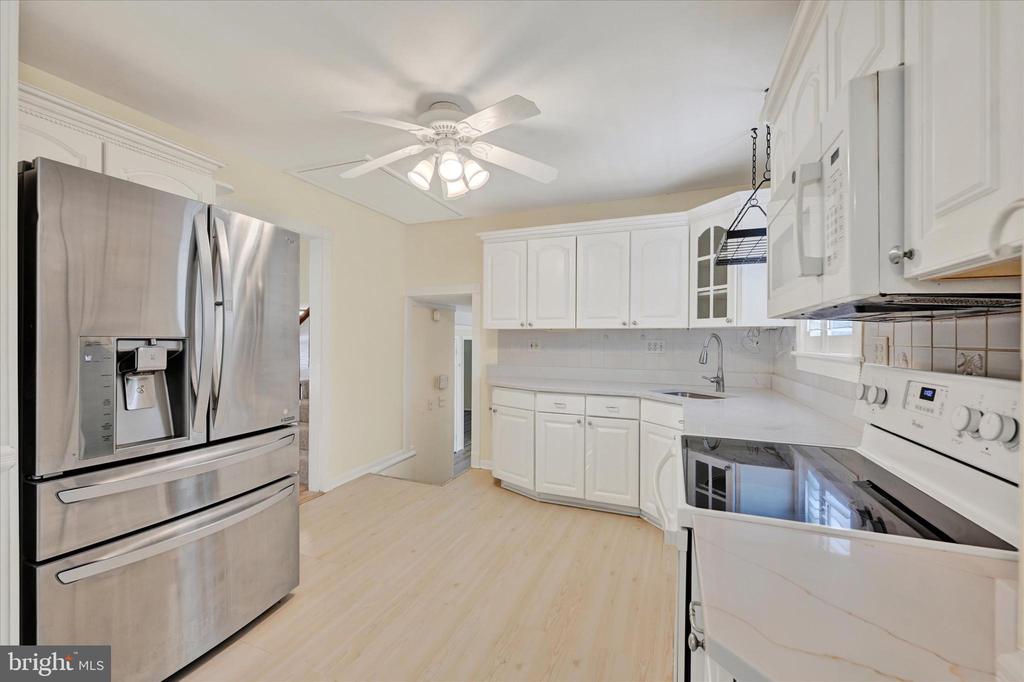 White kitchen with stainless steel appliances, a ceiling fan, and pale wood flooring.