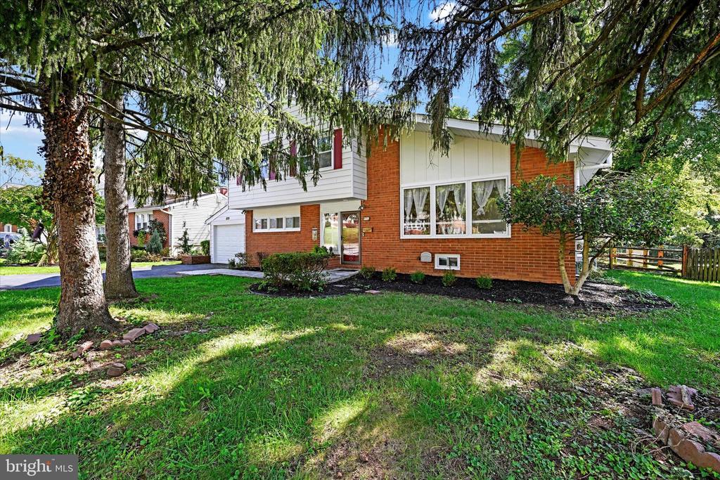Split-level brick and white-sided home framed by mature trees, with a broad lawn and attached garage.