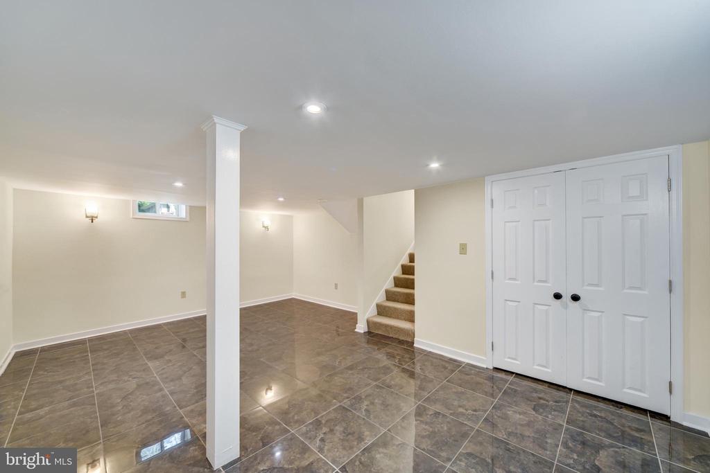 Finished basement with glossy tile floors, a white support column, closet doors, and carpeted stairs.