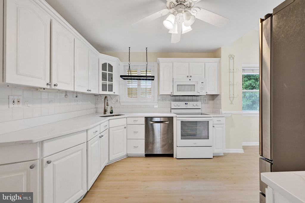 Kitchen with white cabinets, stainless steel dishwasher, white appliances, and light wood floors.