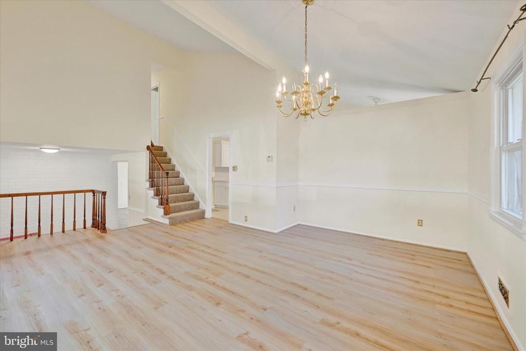 Vacant living room with pale wood floors, a brass chandelier, and staircase.