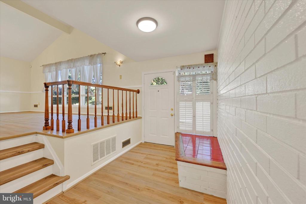 Entry foyer with wood flooring, a white front door, and stairs beside a raised living area.