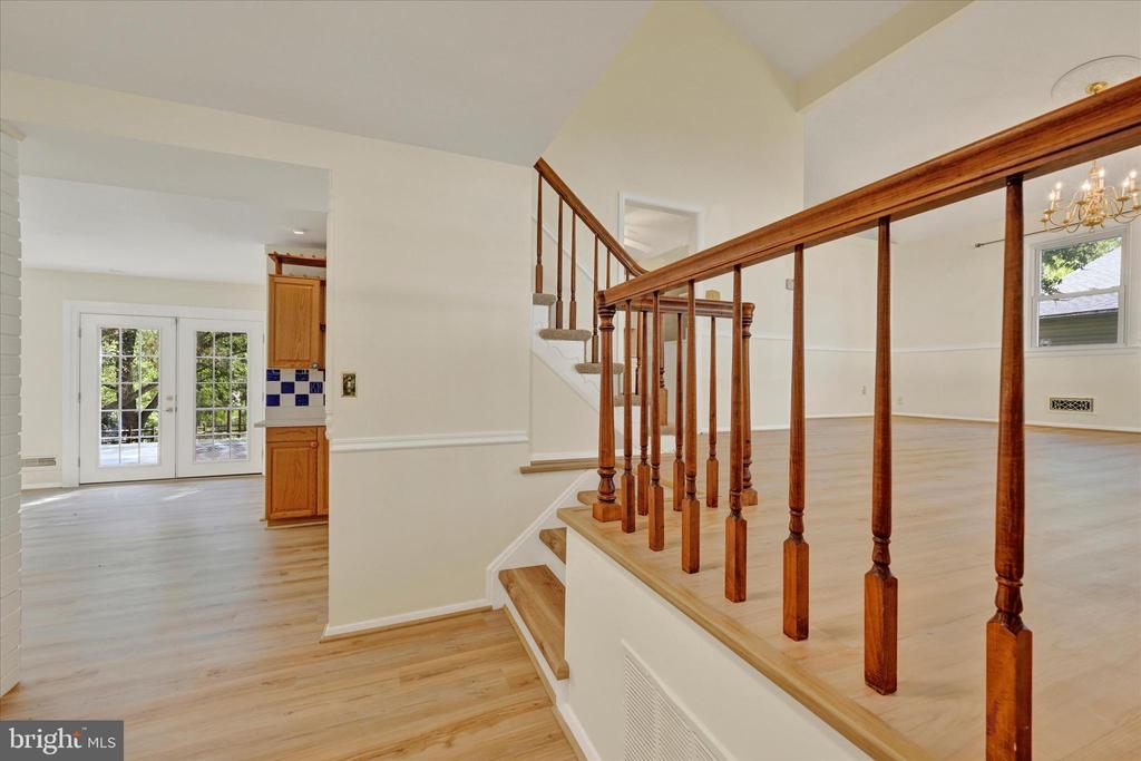 Open split-level interior with hardwood floors, a polished wood railing, stairs, and French doors.