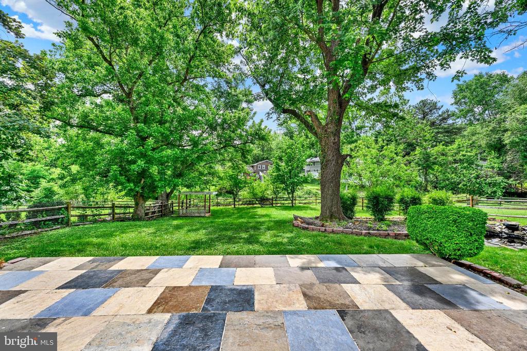Backyard with a multicolored stone patio, mature shade trees, lawn, and wooden fence.