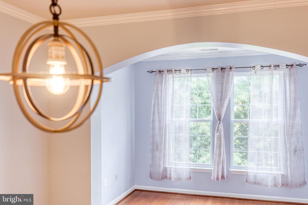 Empty room with hardwood floors, an arched opening, and two curtained windows.