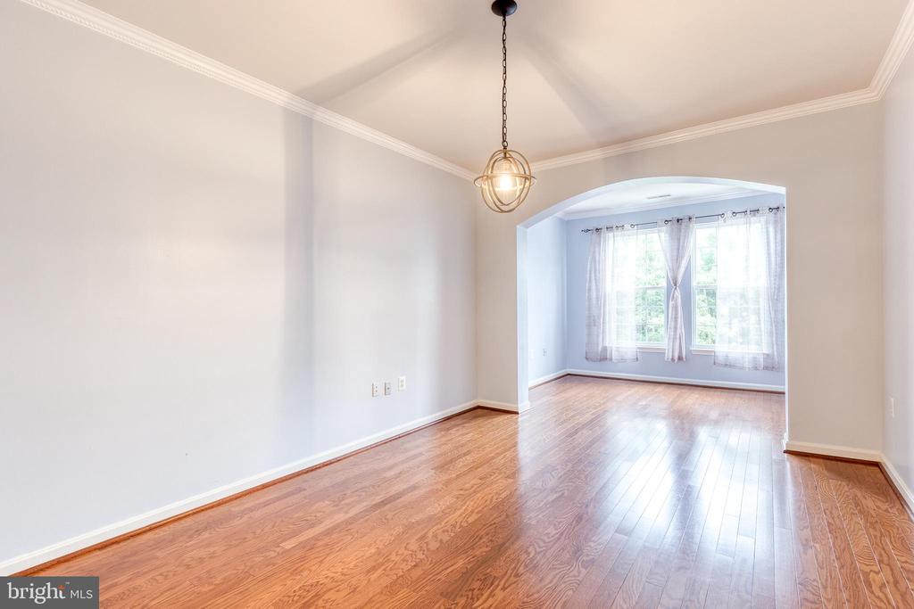 Empty dining room with hardwood floors and an arched opening to a bright windowed alcove.