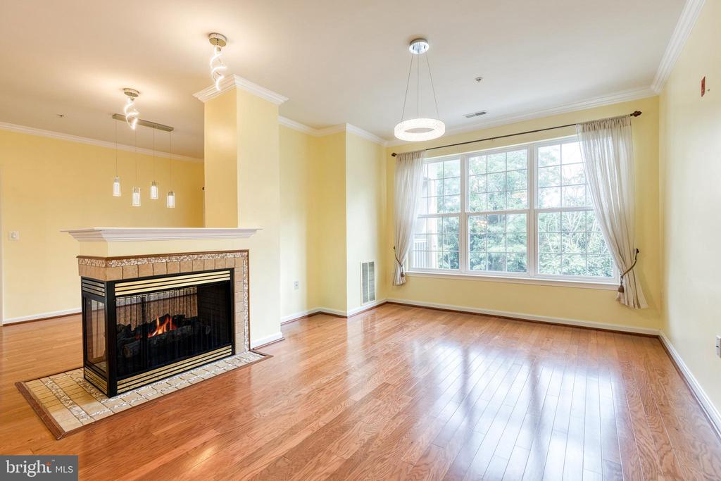Empty living room with a tiled fireplace, hardwood floors, and a large curtained window.